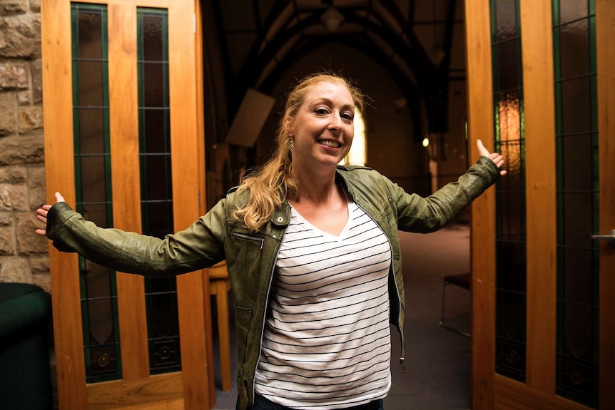Deborah Brennan holds her arms out wide inside a church building.