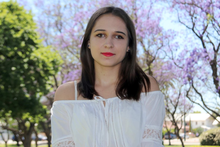 Vanessa Vlajkovic stands in front of some jacaranda trees.