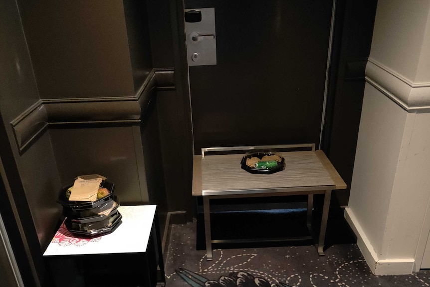 Small tables placed at the entrance of hotel rooms. Empty food containers sit on the tables at each door.