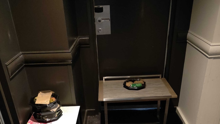 Small tables placed at the entrance of hotel rooms. Empty food containers sit on the tables at each door.