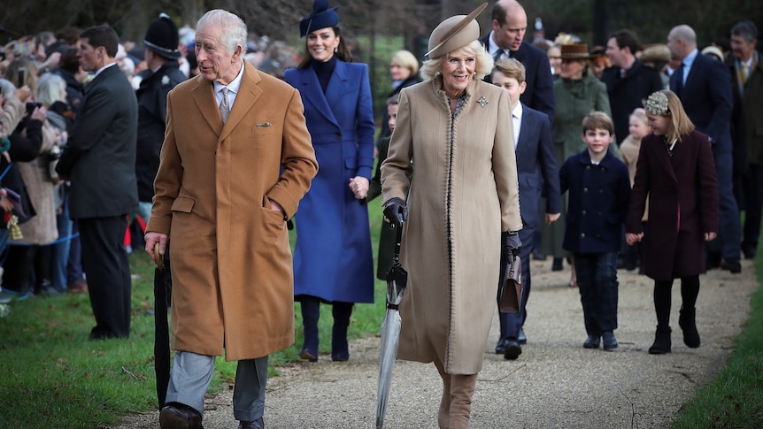 King Charles and Queen Camilla hold their umbrellas as they walk on a path with Catherine, William and their grandchildren.