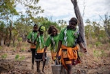 Students carry buckets of water through the bush