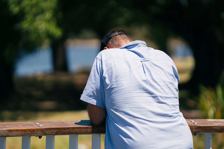 A man leans on a railing, looking down. His face is not visible.