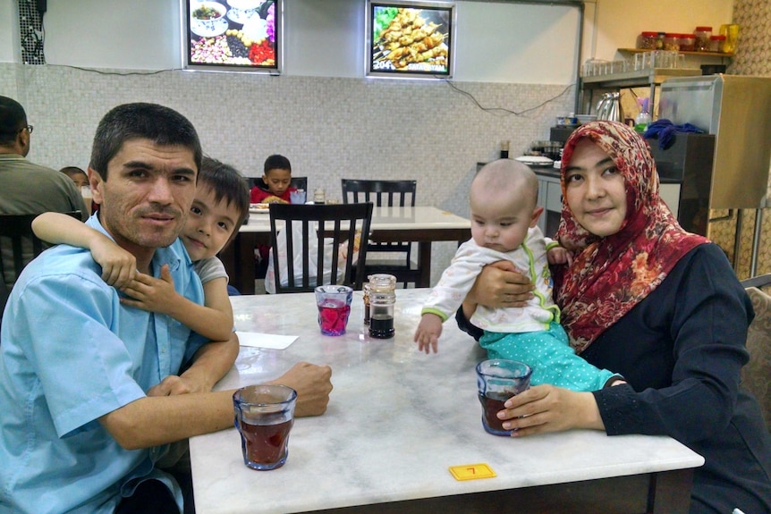 Mamutjan Abdurehim, far left, sits at a table in a restaurant his wife and two children.