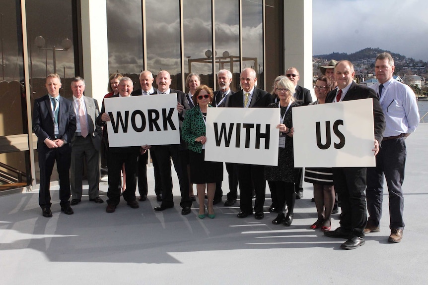 Tasmanian mayors pose with placards urging the minister to "work with us"