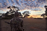 A man stands in silhouette at dawn with a rifle