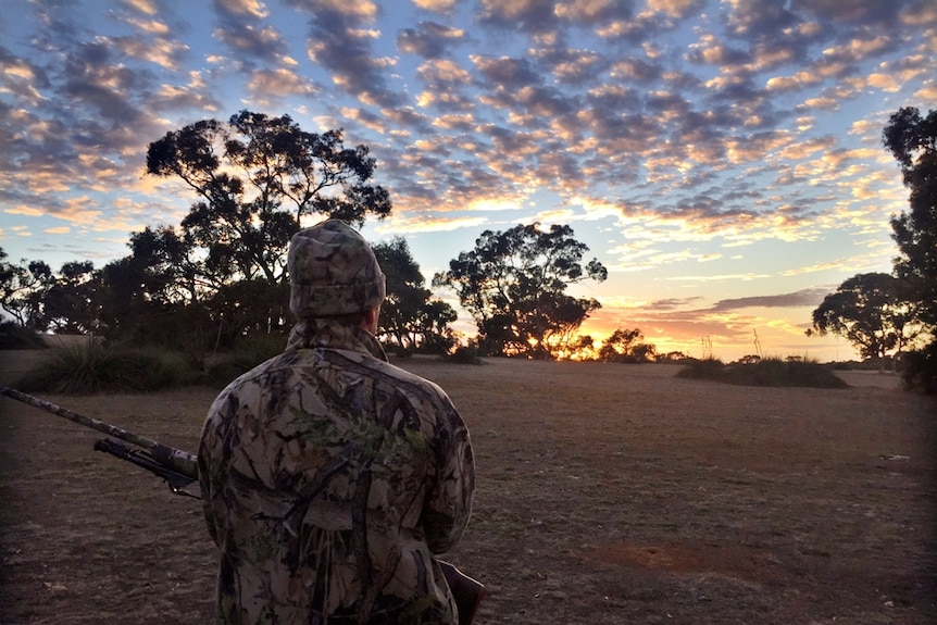 A man stands in silhouette at dawn with a rifle