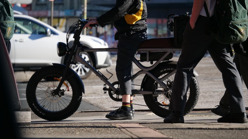 A person in a school uniform sits on a fat-tyred e-bike.