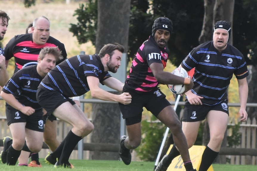 A player tackles another holding a white rugby ball.