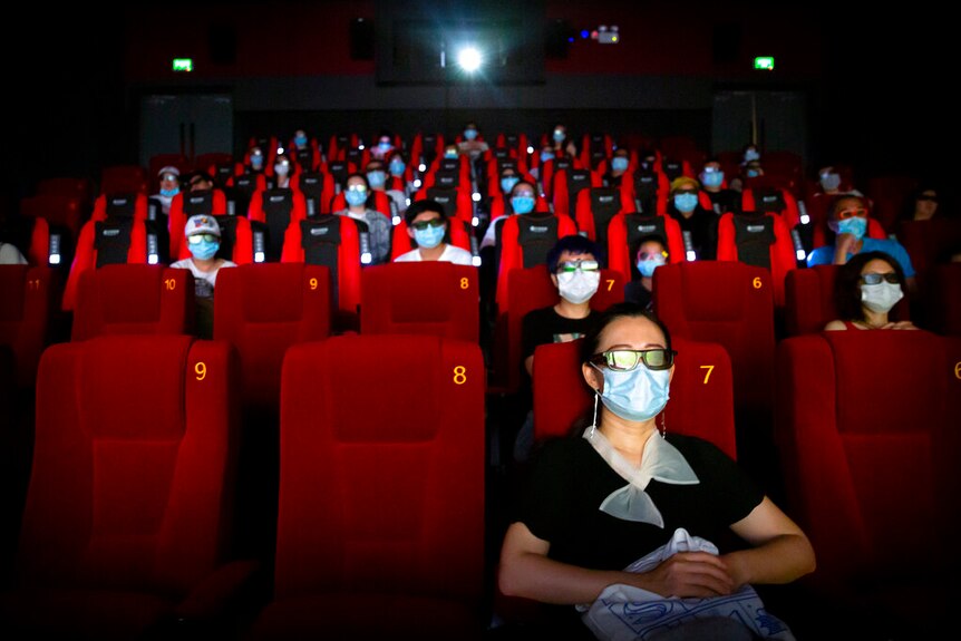 戴着口罩的人们坐在中国的电影院里。