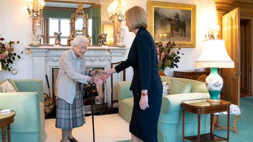 the Queen stands with a walking stick and shakes new PM Liz Truss's hand.