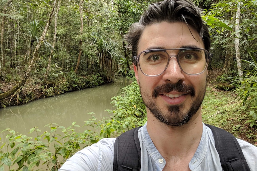 A young man wearing glasses takes a selfie in the jungle