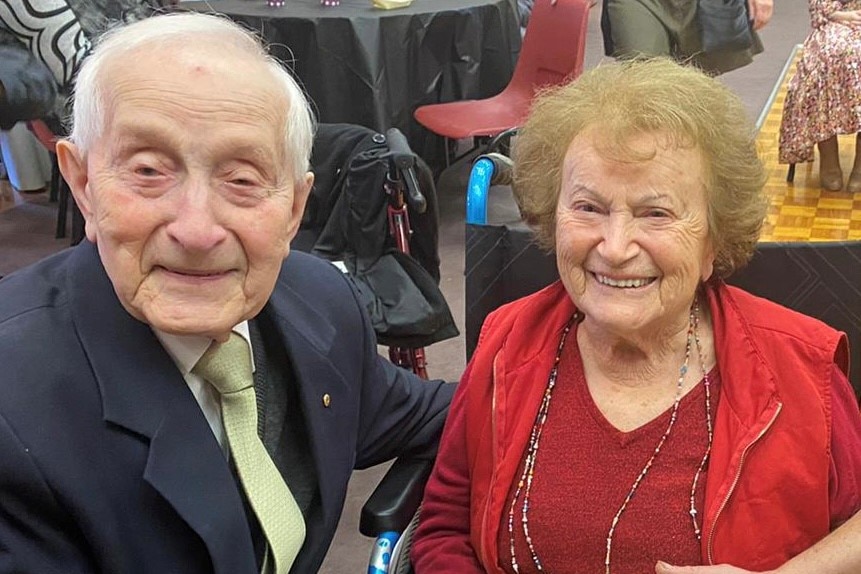 Abram Goldberg sits next to wife Cesia, both smiling widely, with a green cake with '75' on it between them.