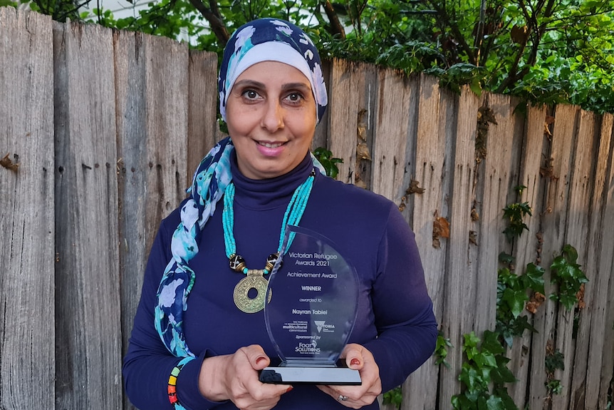 Nayran Tabiei holds her prize and smiles for the camera, wearing a blue top and a blue hijab. 