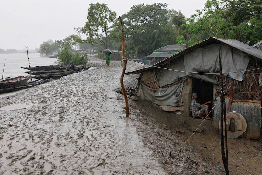 A woman can be seen sitting in a small house on the banks of a water dam while it rains.
