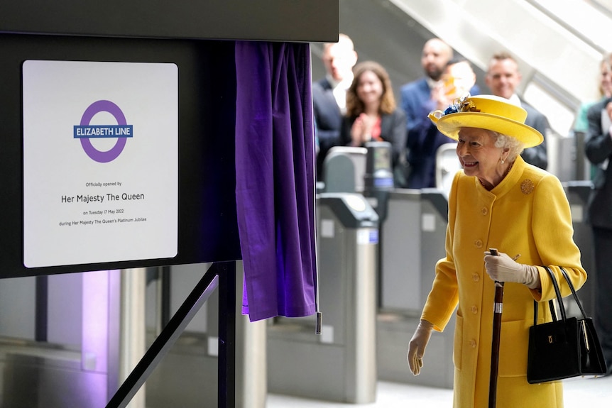Queen smiles in front of curtain plaque for train 