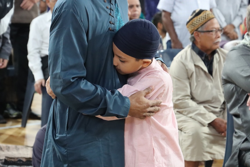 A boy hugging a man, with other people in the background, at a prayer service.
