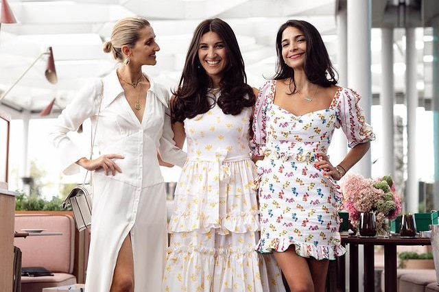 Three women in sundresses posing for a photo in a sunny restaurant
