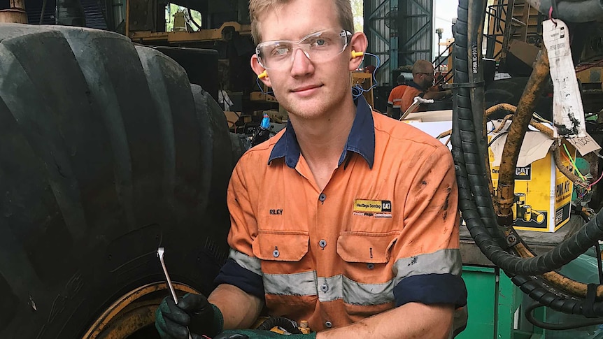 a young man holding a spanner next to a big machine