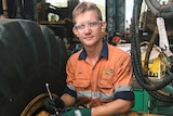 a young man holding a spanner next to a big machine