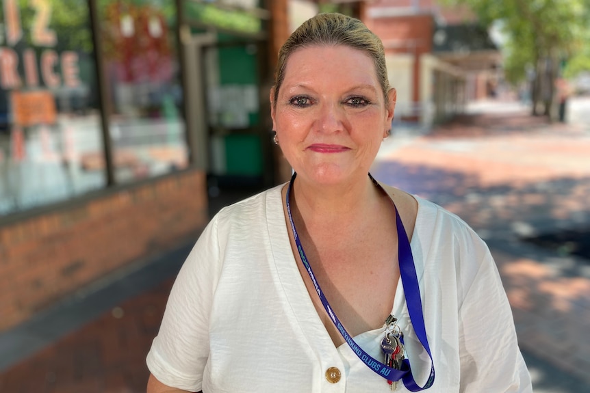 A middle-aged woman wearing white top, pulled back hair and a lanyard around her neck, smiles at the camera.