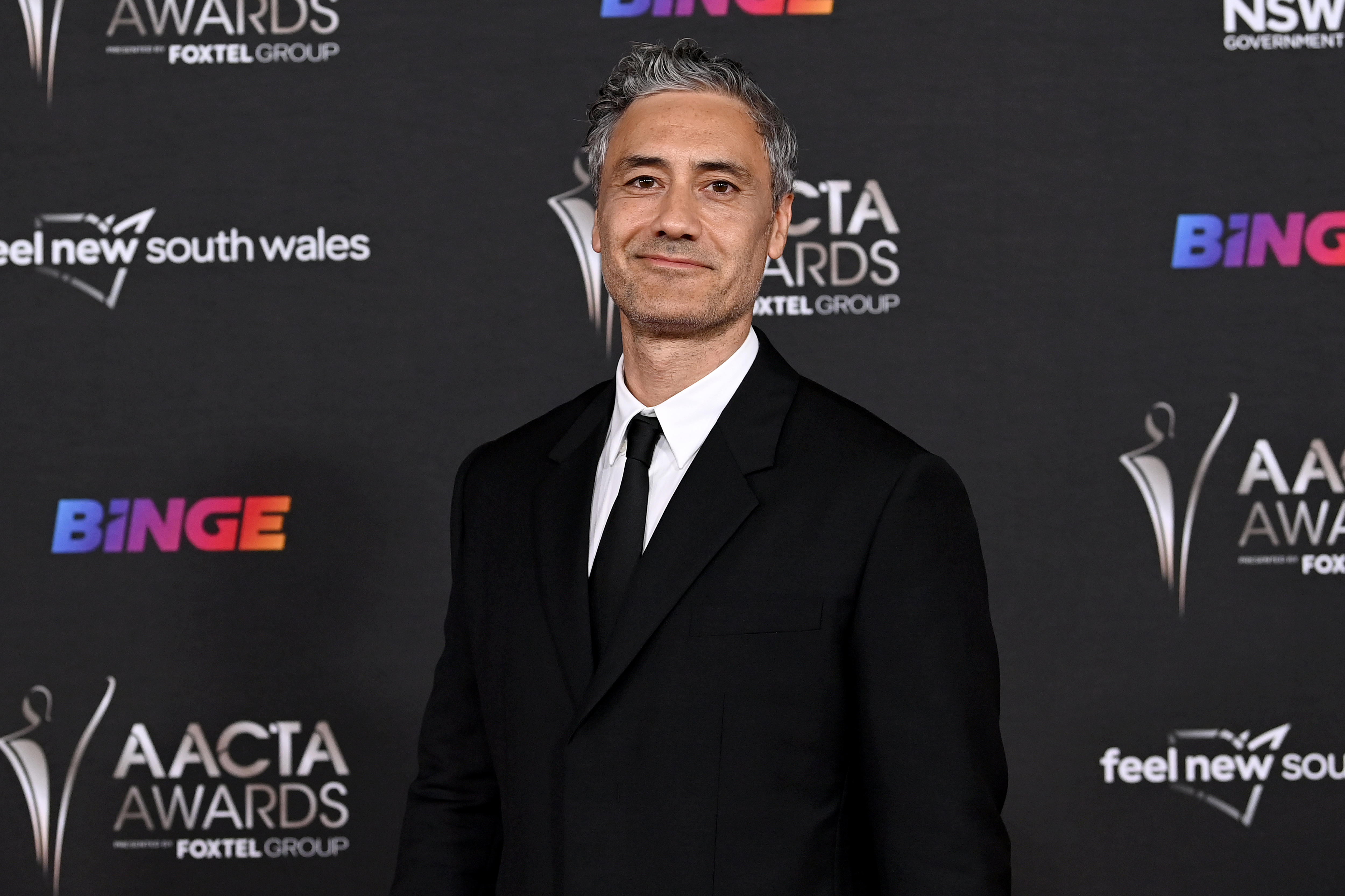 A man with short black and grey hair wearing a black tux in front of a sponsorship wall 