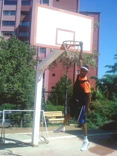 A young teenager uses one arm to hang from the rim of a basketball hoop.