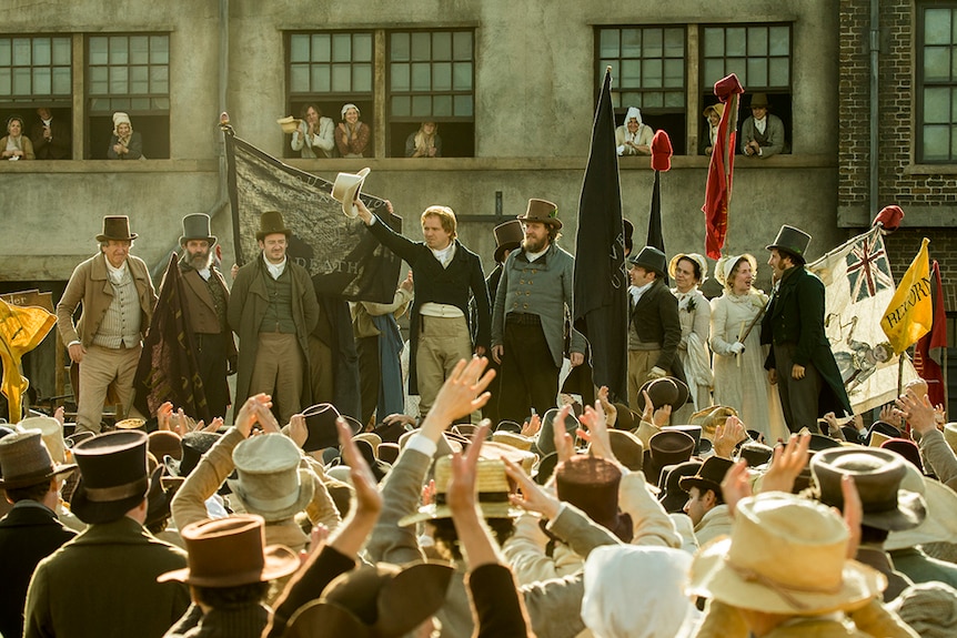 Colour still of Neil Bell, John-Paul Hurley, Philip Jackson, Rory Kinnear, and Tom Gill addressing crowd in 2018 film Peterloo.