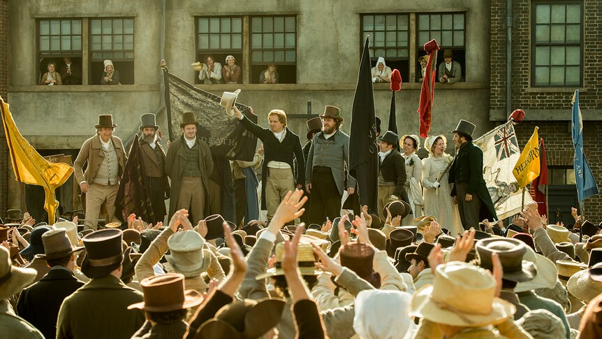 Colour still of Neil Bell, John-Paul Hurley, Philip Jackson, Rory Kinnear, and Tom Gill addressing crowd in 2018 film Peterloo.