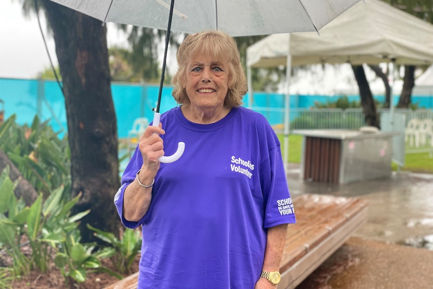 An elderly woman holds an umbrella, smiling