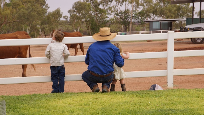 Angus Mackay crouches with his children by a fence.