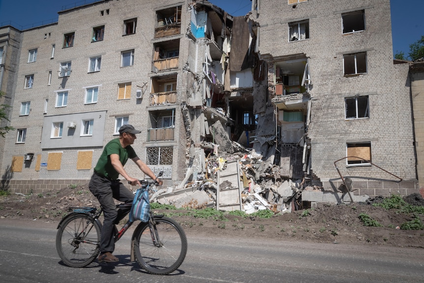 A man rides a bicycle past a building damaged in Russian shelling