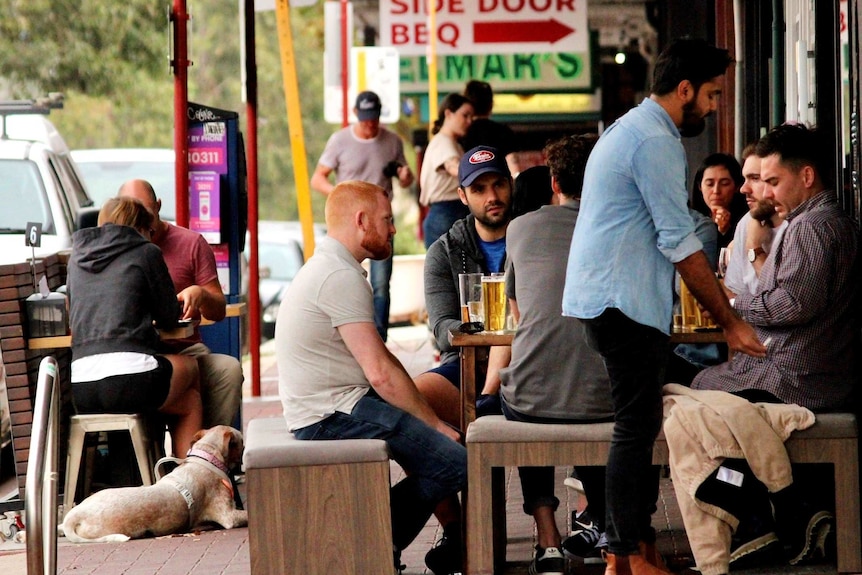 A group of men sit at a pub table with beers on a Perth street, with a dog lying on the ground in the background.