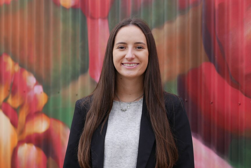 A young woman standing in front of a bright pink mural