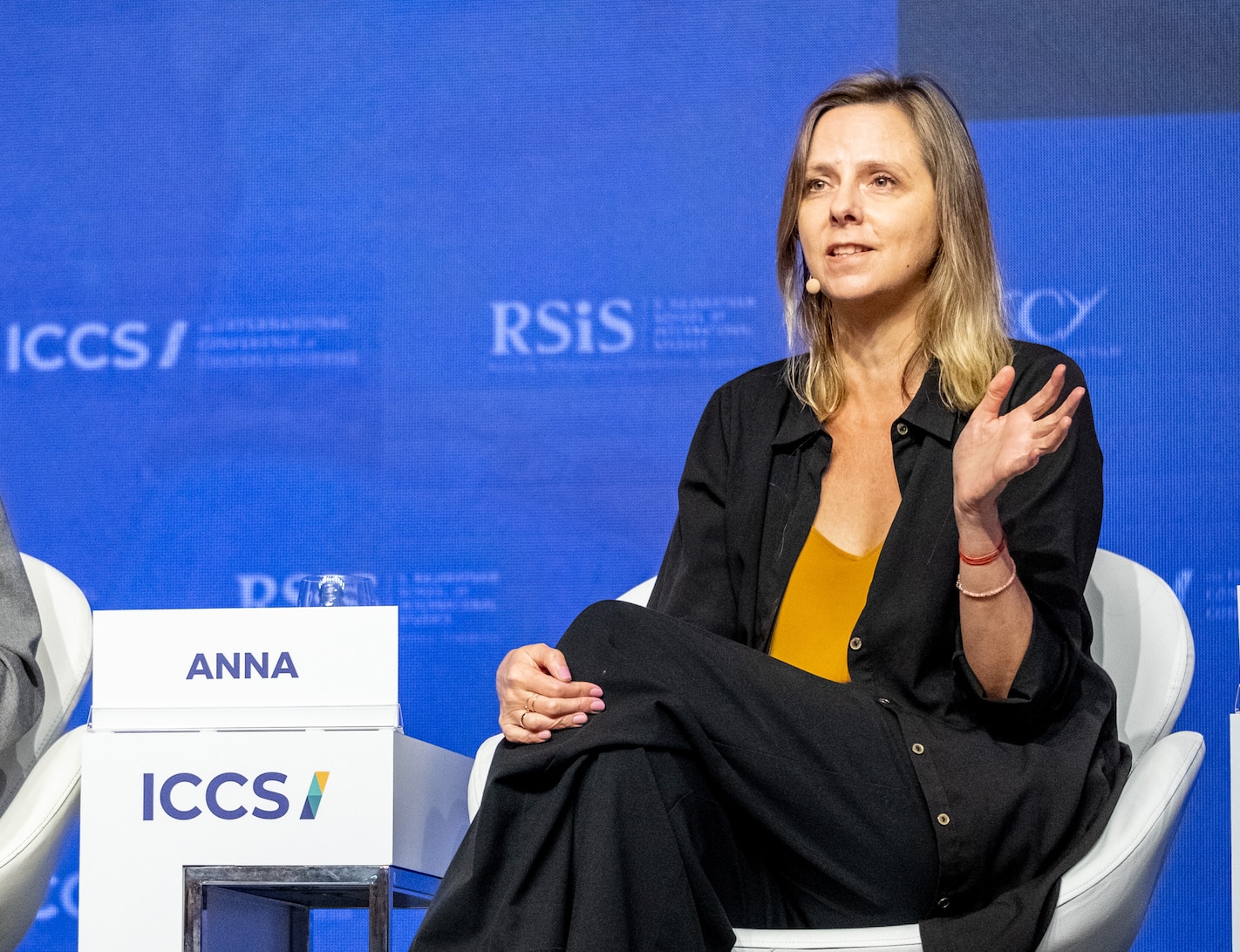 A woman with long hair sits on a stage speaking
