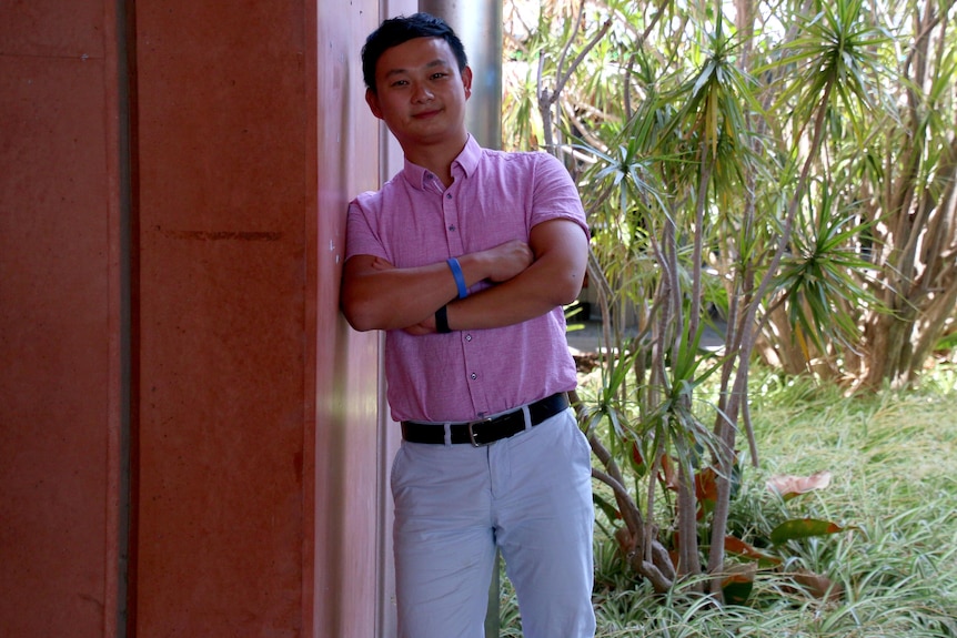 Dr Cheng leans against a wall with his arms folded. 