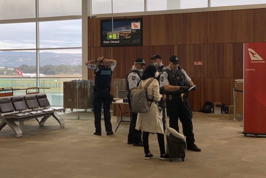 Police at Adelaide Airport wear face masks with a solitary passenger.