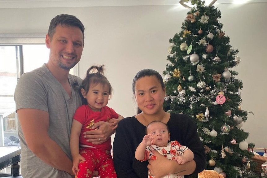 A family of two adults and two young children smile for a Christmas photo.