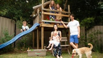 A family stand and sit in front of play equipment with a dog in the foreground.