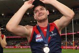Angus Brayshaw holds the tip of his cap and smiles. A premiership medal is around his neck
