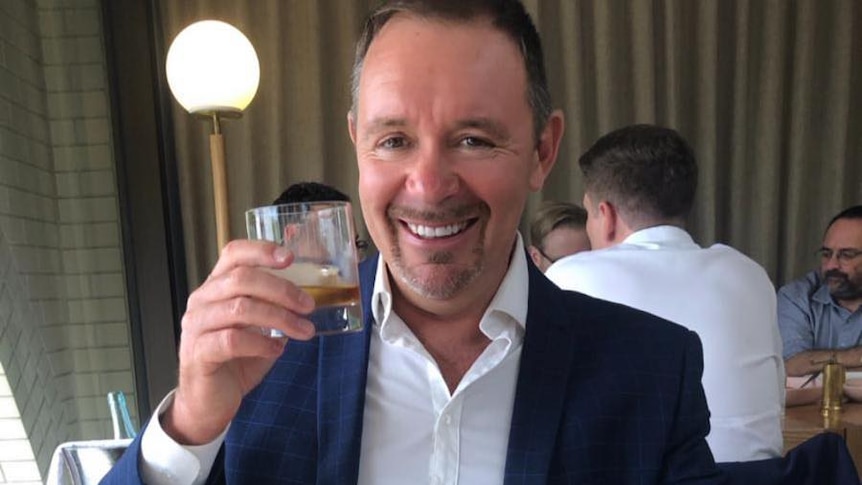 man sits in blue suit cheerings glass