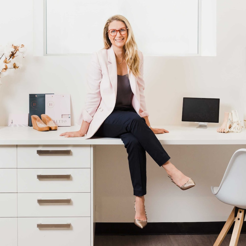 A woman sits on a desk with her legs crossed.