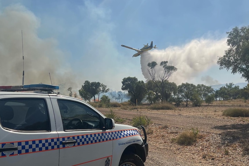 A water bomber plane drops water on grass fire