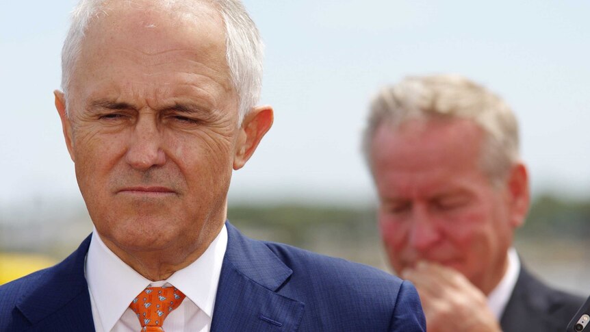 A head shot of Malcolm Turnbull looking downwards with an out-of-focus Colin Barnett in the background.