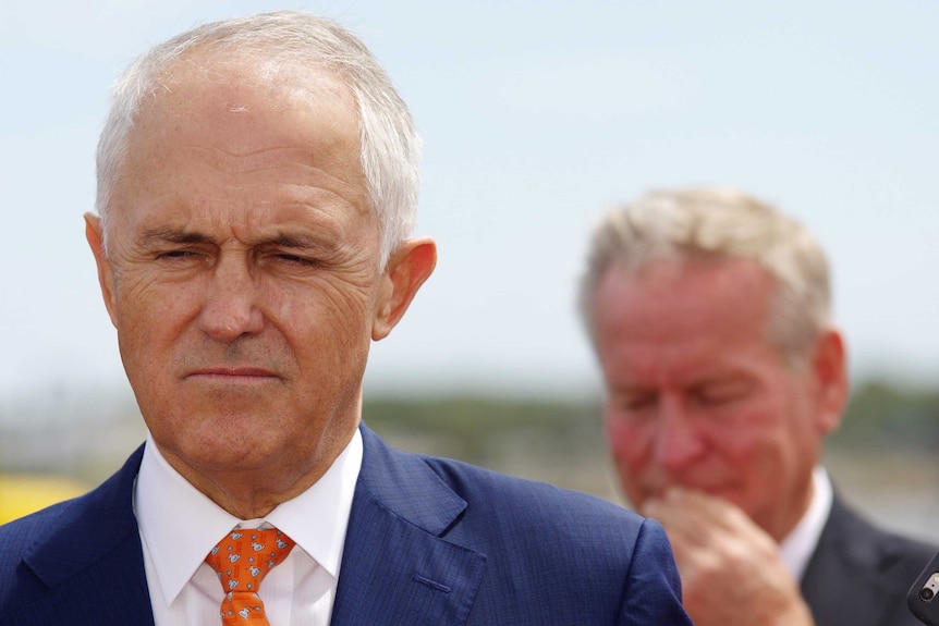 A head shot of Malcolm Turnbull looking downwards with an out-of-focus Colin Barnett in the background.