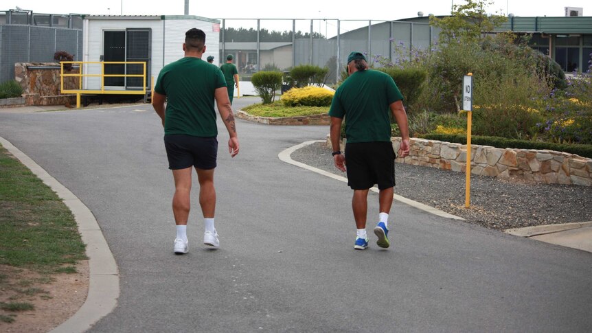 Two prisoners wearing green uniforms walk in a fenced area at Fulham Correctional Centre.