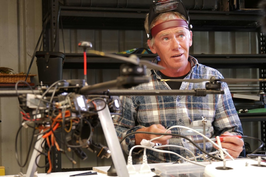 Dave sits in his shed near a drone holding a soldering iron