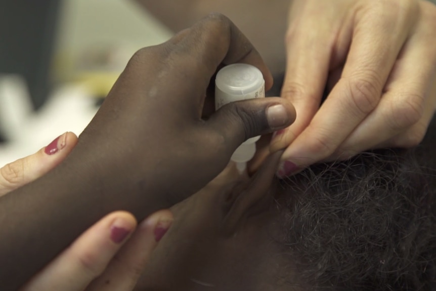 An Aboriginal girls places liquid into her ear with the help of a female researcher.