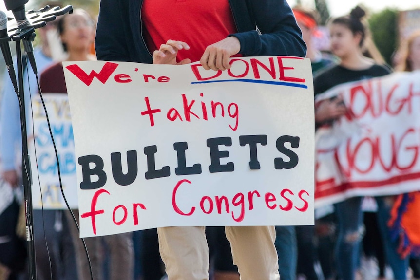 A student holds a sign reading 'we're done taking bullets for Congress'