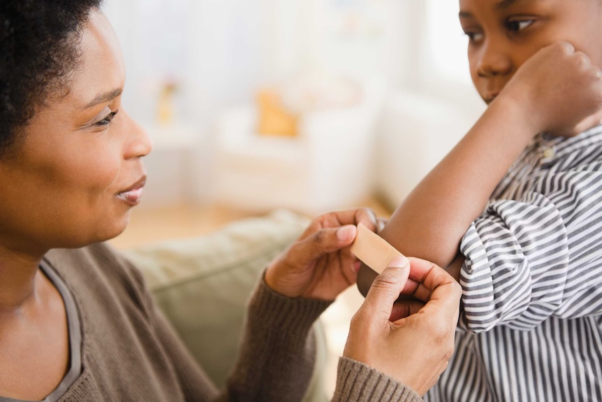 Une mère pose un sparadrap sur le coude de son fils.'s elbow.